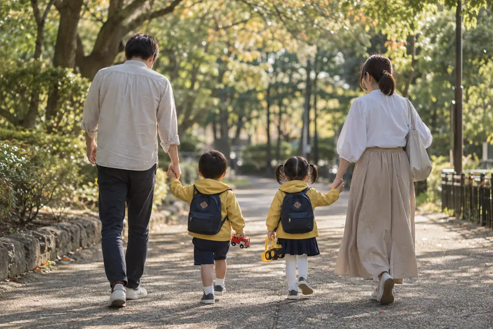 平日の午後、ミニカーを持った双子コーデの3歳の男女の双子と手をつないで公園を歩く両親の後ろ姿（イメージ）